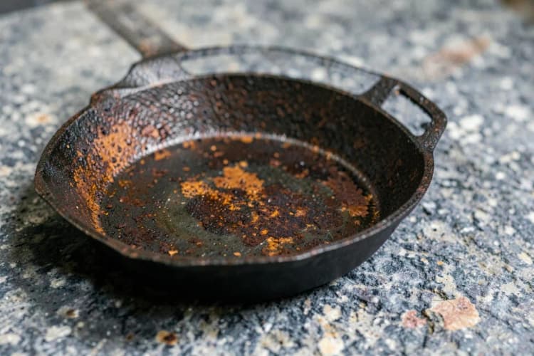 Uma panela de ferro fundido com manchas de ferrugem, em uma bancada de pedra cinza.